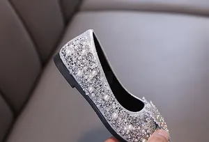 Close-up of silver girls princess shoes with sparkling rhinestones and white pearls.