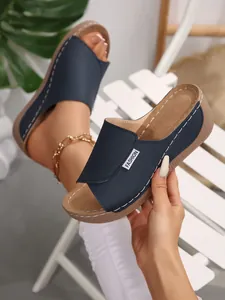 Close-up detail of navy blue peep-toe wedge sandals featuring a wide strap and fashion label