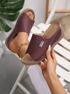 Detail view of burgundy wedge heel slippers with wide strap and fashion label