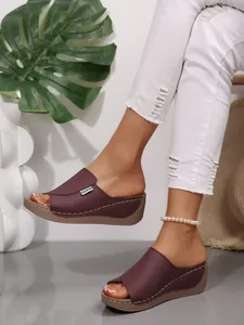 Close-up of stylish burgundy peep-toe wedge slides worn with ripped white jeans