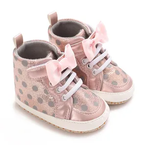 Vue détaillée de chaussures bébé roses à paillettes avec pois et un nœud papillon.