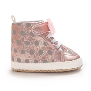Nahaufnahme eines rosa Glitzer-Babyschuhs mit grauen Punkten und einer Schleife.