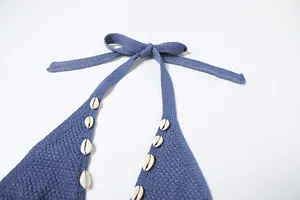 Detailed macro view of blue knitted halter dress featuring white cowrie shell accents