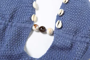 Macro view of blue knitted dress neckline featuring white shell accents and marble beads