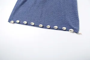 Close-up detail of blue open-knit dress featuring decorative cowrie shell beads on the hem.