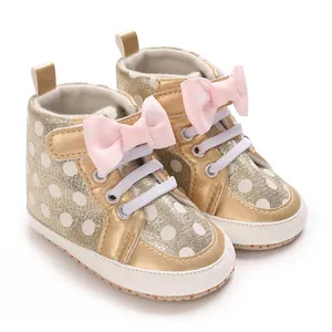 Gros plan de chaussures dorées pour bébé avec nœuds roses et motif à pois blancs