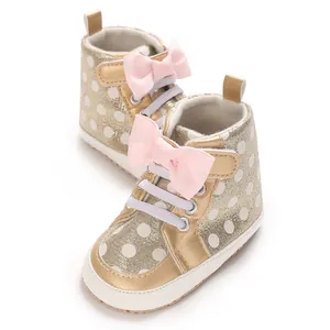 Détail des chaussures de marche pour bébé dorées à pois avec un joli nœud rose doux
