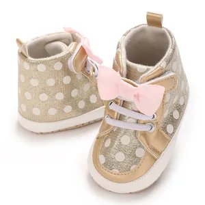 Gros plan de chaussures de marche pour bébé dorées à pois avec de jolis nœuds roses