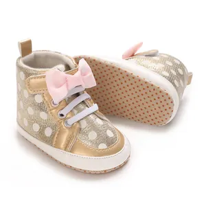 Détail de chaussures bébé dorées à pois avec nœud rose et semelle souple