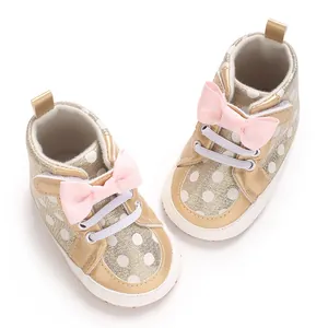 Chaussures bébé dorées à paillettes avec nœud rose et motif à pois blanc en détail.