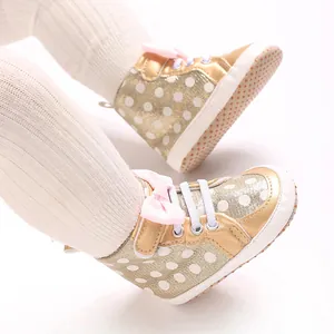 Gros plan détaillé de chaussures de marche dorées pour bébé avec des pois et un nœud rose.