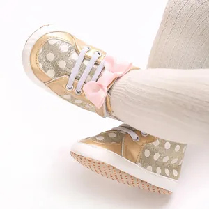 Gros plan de chaussures bébé dorées à pois avec un nœud rose et une semelle souple