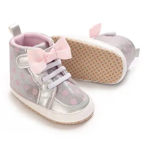 Détail de chaussures bébé argentées avec nœud rose et semelle souple antidérapante.