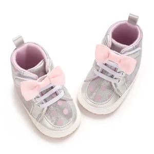 Gros plan de chaussures bébé argentées avec des pois roses et un nœud décoratif.
