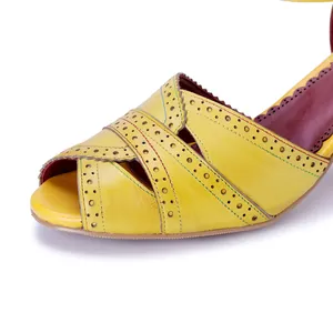 Primo piano di sandali in pelle vintage gialla con dettagli brogue e cinturini traforati