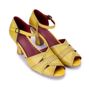 Dettaglio di sandali vintage in pelle gialla con intagli smerlati e cinturini incrociati.