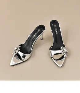 Detail von silbernen Mules mit glitzernden Strass-Blumendekorationen und Pfennigabsatz.