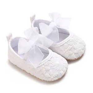 Detailansicht weißer Babyschuhe aus Spitze mit dekorativer Seidenschleife und Stickerei.
