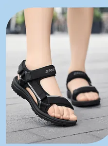 Niño con sandalias deportivas negras de exterior con correas ajustables en el suelo.