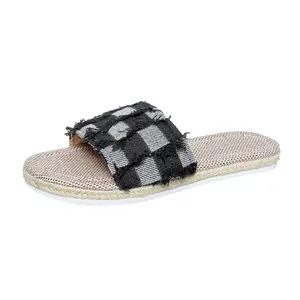 Close-up of checkered denim flat slide sandal with frayed edges and woven sole
