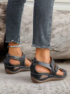 Detail view of black wedge sandals with hook and loop straps and white stitching.