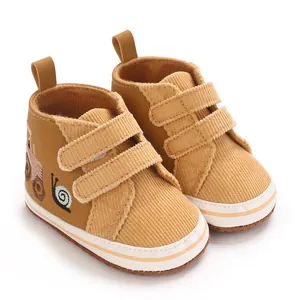 Primer plano de zapatos de bebé en pana color mostaza con un lindo bordado de caracol