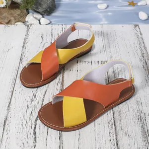 Sandalias planas de mujer con tiras cruzadas naranja y amarillo sobre madera blanca.