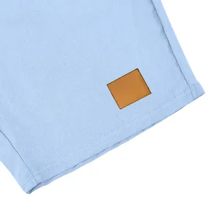 Primo piano di pantaloncini in lino celeste con dettaglio toppa in pelle marrone