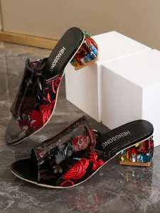 Detalle de sandalias negras para mujer con bordado floral y tacones de gemas coloridas.