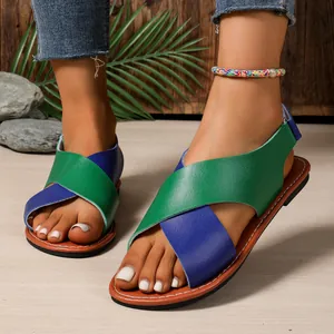 Primer plano de sandalias planas con correas cruzadas verdes y azules y tobillera.
