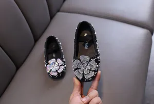 Close-up of rhinestone camellia flower and pearl details on girl's black princess shoes.
