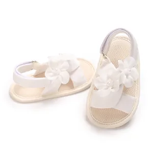 Vue détaillée de sandales pour bébé fille avec fleurs en tissu blanc et brides souples.