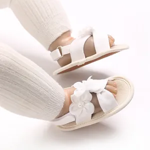 Détail de sandales blanches pour bébé fille avec fleurs délicates et brides croisées.