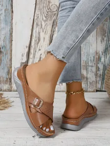 Close-up of brown wedge sandals featuring cross straps and a gold-tone buckle.