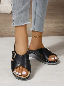 Close-up of black cross-strap wedge sandals with gold buckles and perforated details