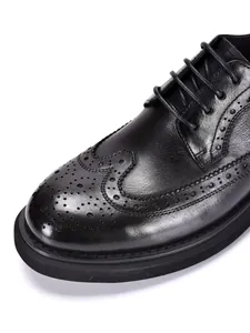 Close-up of black leather brogue shoe with intricate wingtip carvings and thick sole
