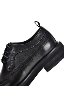 Detailed view of black leather brogue shoes with intricate wingtip perforation and thick sole