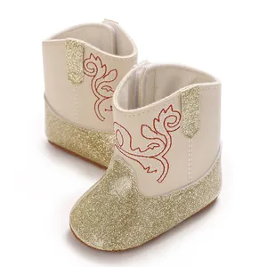 Detailopname van crèmekleurige babyloopschoenen met gouden glitters en borduursel.