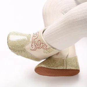 Close-up van baby loopschoentjes met gouden glitter en rode geborduurde details.