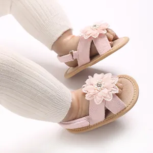 Close-up of pink baby girl sandals with delicate flower and pearl details on white background.