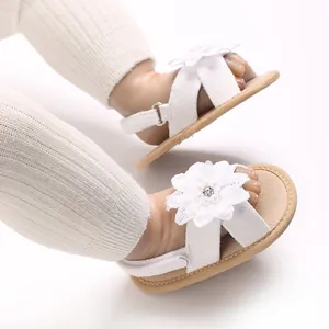 Detailed close-up of white baby girl sandals featuring delicate lace flower and pearl accents