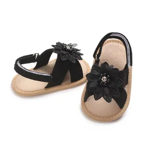 Close-up of black baby sandals with intricate flower decorations and soft beige soles.