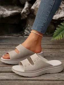 Close-up of beige women's platform slides with elegant rivet details and textured straps