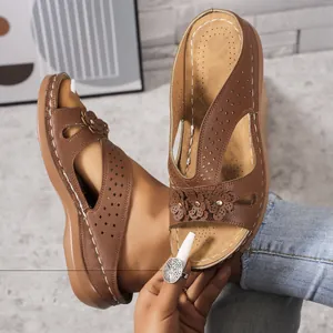 Detail of brown wedge sandals featuring laser-cut patterns and floral rivet accents.