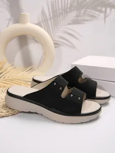 Detail of black platform slide sandals with silver studs and a thick beige sole
