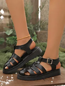 Stylische schwarze römische Sandalen mit dicker Plateausohle am Fuß eines Modells.