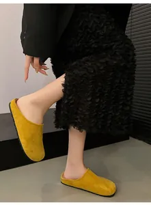 Detailed view of yellow suede closed-toe clogs on model with stylish black outfit.