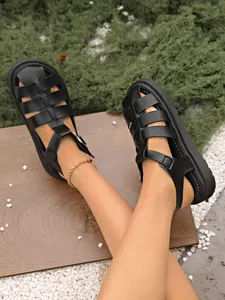 Nahaufnahme von stilvollen schwarzen geflochtenen Fisherman-Sandalen in einem Garten.