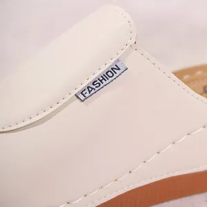 Close-up of beige leather upper with woven FASHION label on summer wedge mules
