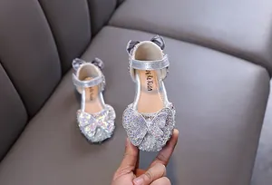 Gros plan de chaussures de princesse argentées pour filles avec un gros nœud papillon en strass.